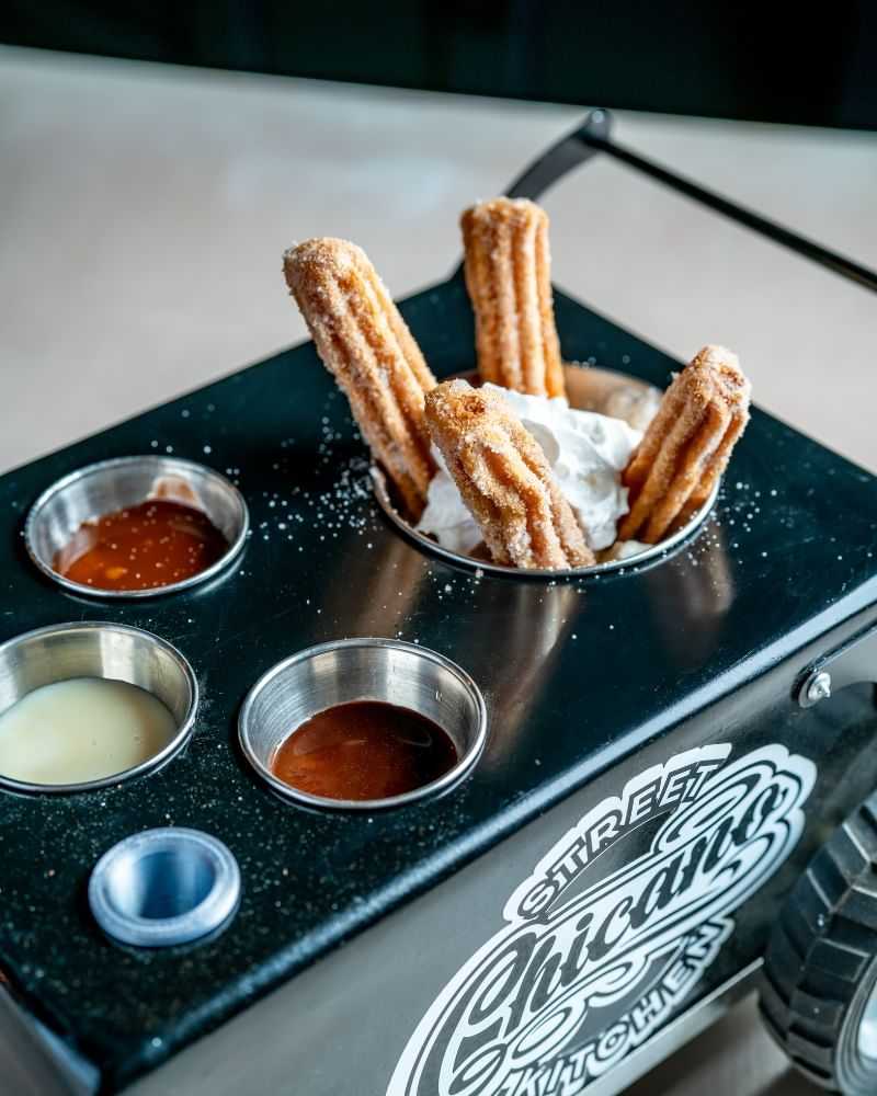 Churros with dipping sauces and whipped cream in a small cart-themed holder.