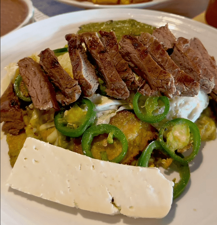 Slices of beef, jalapeños, and cheese served on a bed of grilled vegetables and sauce.