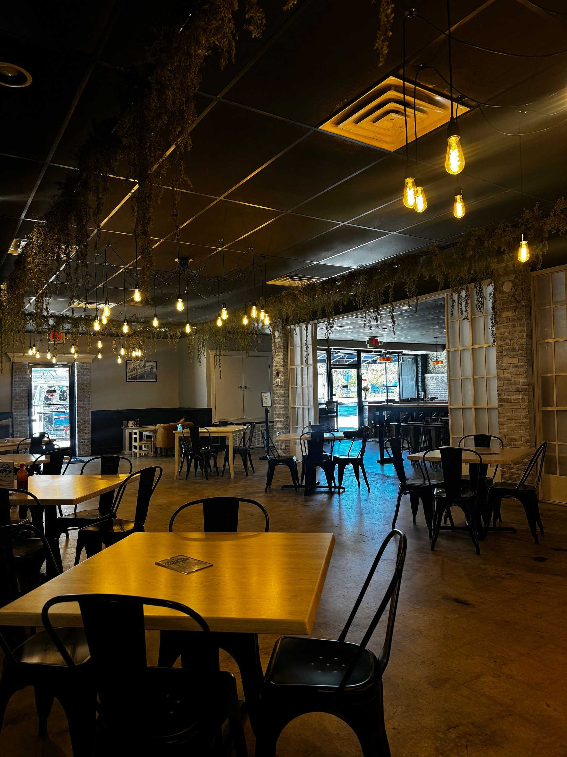 Cozy café with modern decor, hanging lights, wooden tables, and metal chairs in a dim-lit setting.