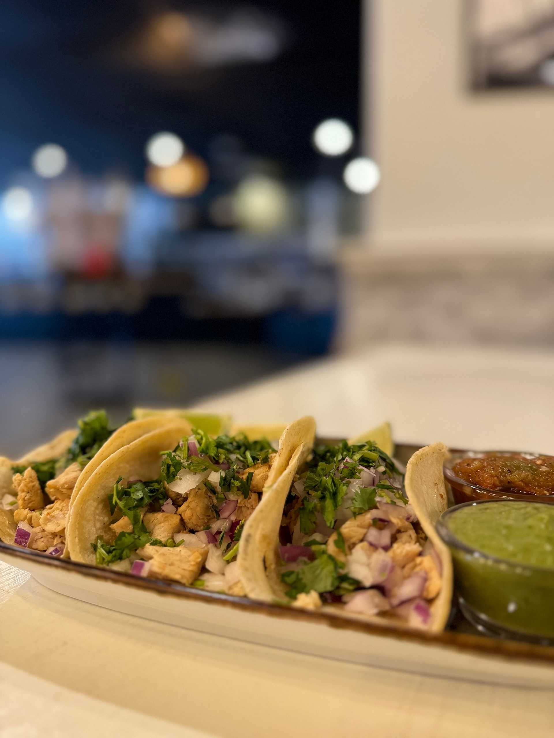 Three chicken tacos garnished with cilantro and onions, served with green and red salsa on the side.