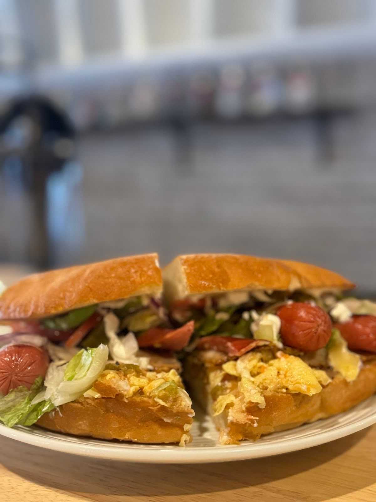 Close-up of a gourmet sandwich with vegetables, sliced sausage, and cheese on a white plate.