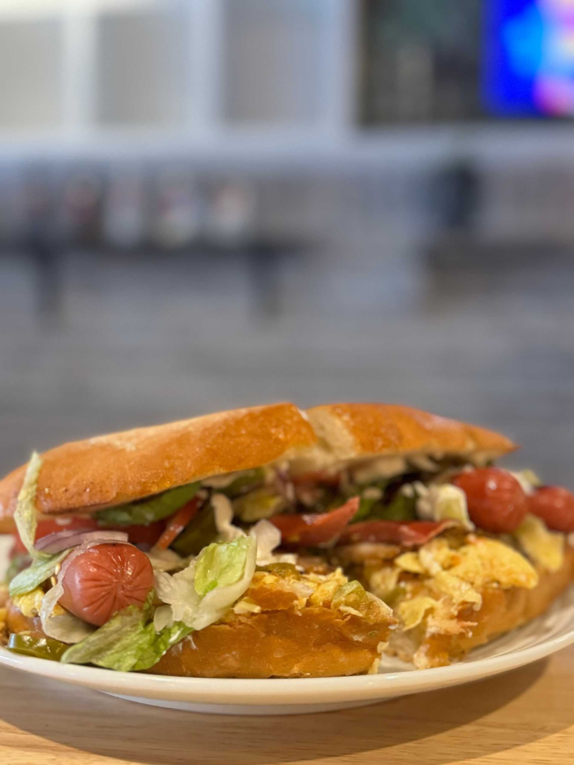 Plate with a loaded sandwich filled with sausages, lettuce, and sliced vegetables.