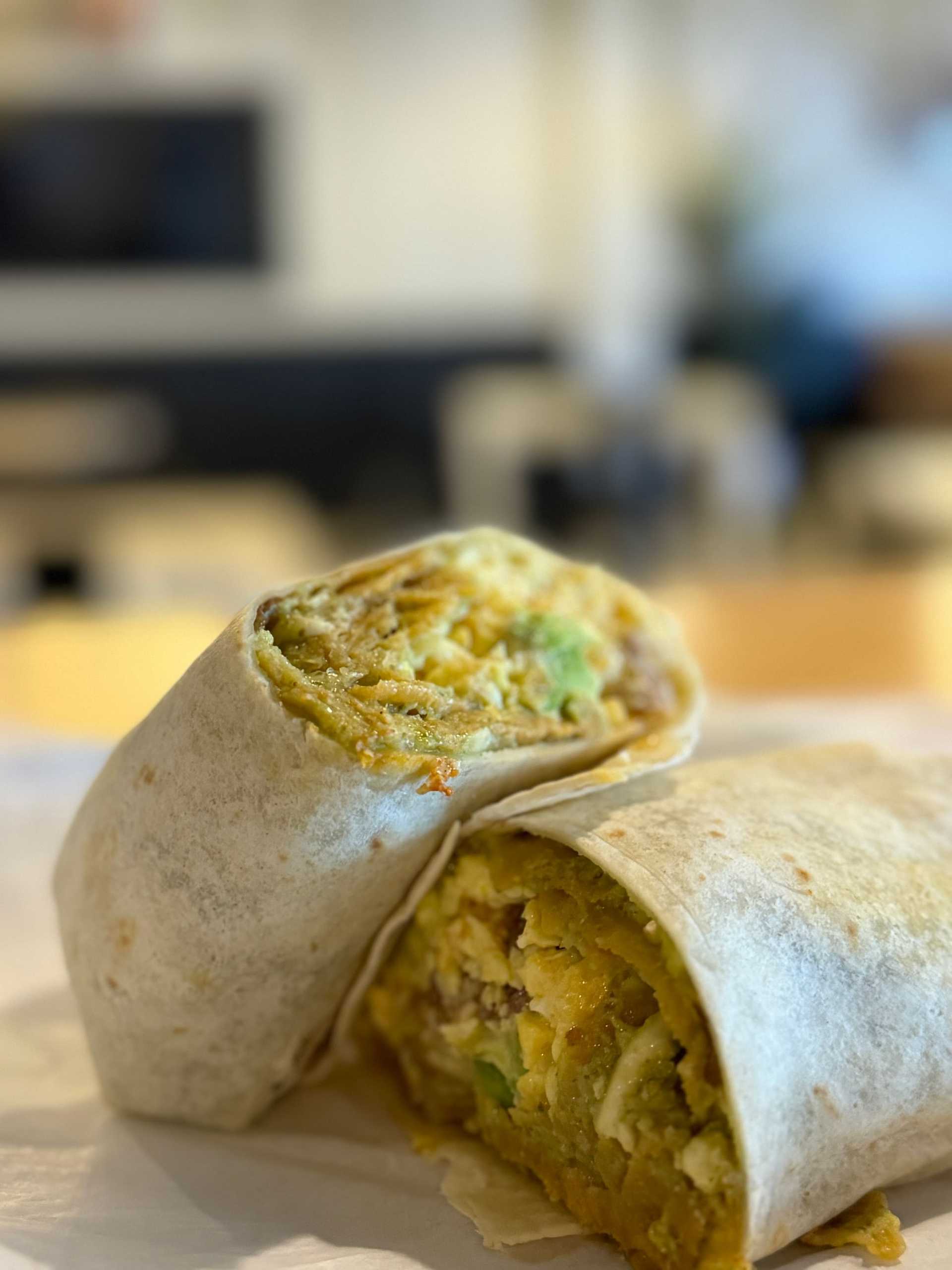 A close-up of a breakfast burrito filled with scrambled eggs, avocado, and other ingredients.