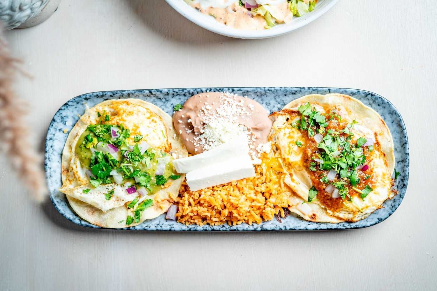 Three enchiladas with beans, rice, cheese, and cilantro on a speckled plate.
