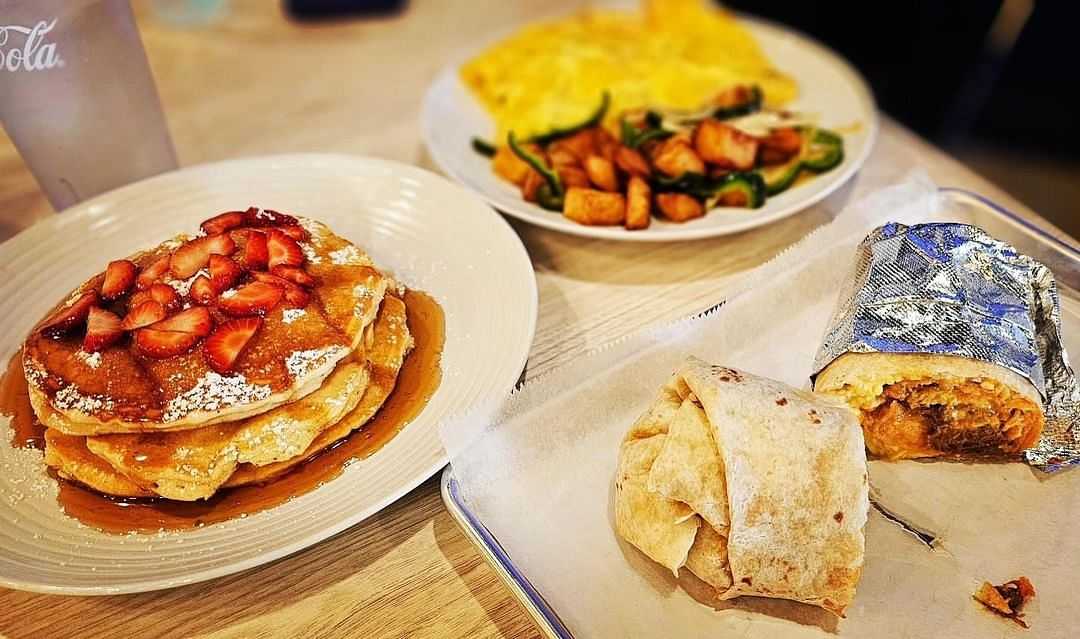 A breakfast spread of pancakes with strawberries, a breakfast burrito, and an omelet with potatoes.